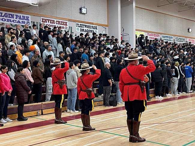 Photo of three officers in red serge saluting with a large crowd in the bleachers.